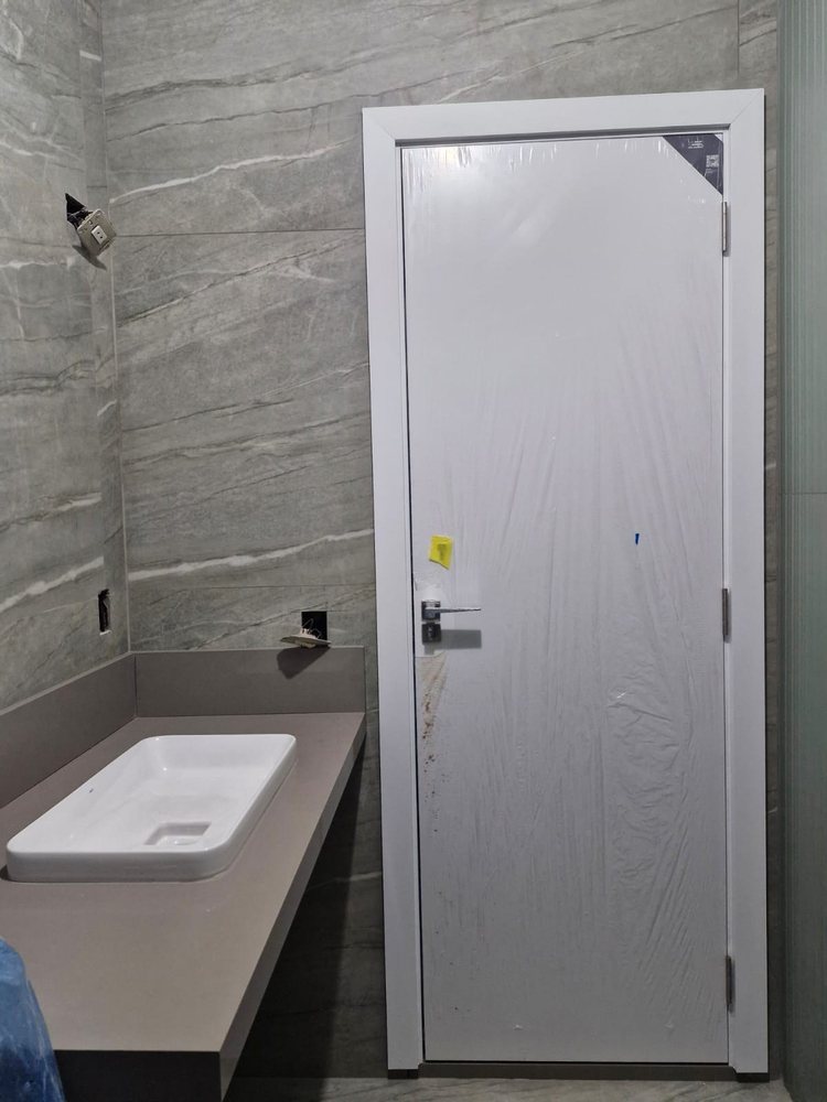 Porta branca com batente branco e puxador cromado, instalada em banheiro revestido de porcelanato cinza