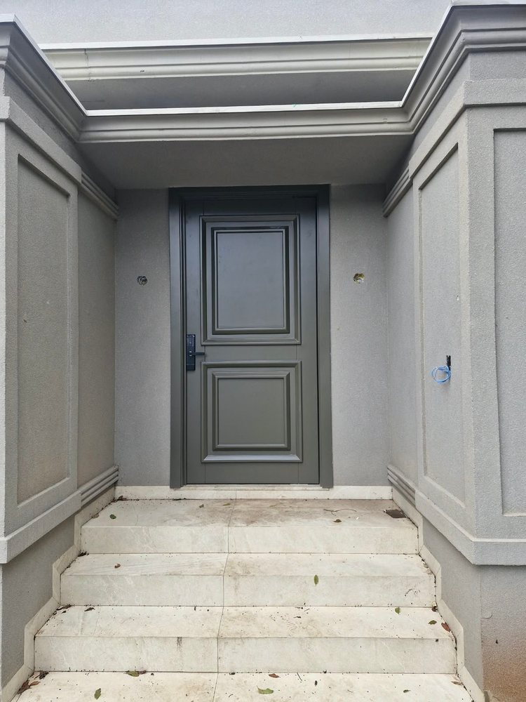 Porta de entrada pintada de verde, com dois painéis em relevo e fechadura eletrônica, instalada em nicho revestido
